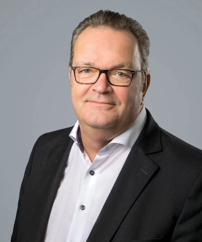 Ein Kollege steht bereit, um über seine Arbeit zu sprechen. Die Hände locker an der Seite, Blick offen in die Kamera.