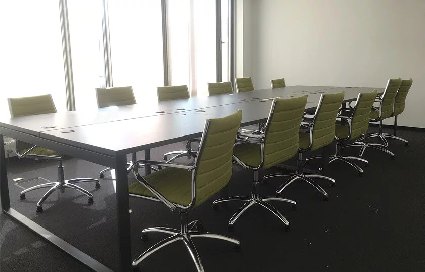 Besprechungsraum: Mitarbeitende arbeiten am langen Tisch, stimmen Projekte ab. Große Fenster bringen Tageslicht ins Meeting.