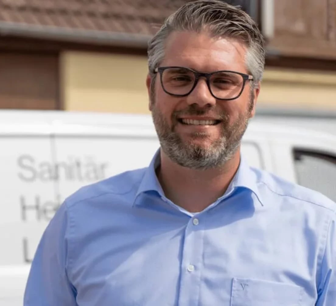 Ein Handwerker steht draußen vor seinem Firmenwagen und bereitet sich auf den nächsten Einsatz vor.