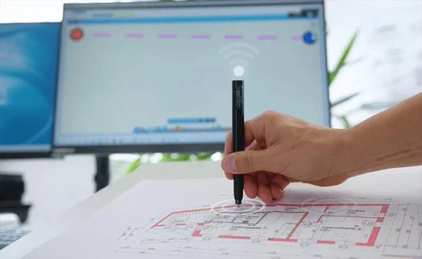 Jemand bearbeitet einen Bauplan mit einem digitalen Stift, am Schreibtisch läuft passende Software auf dem Rechner.